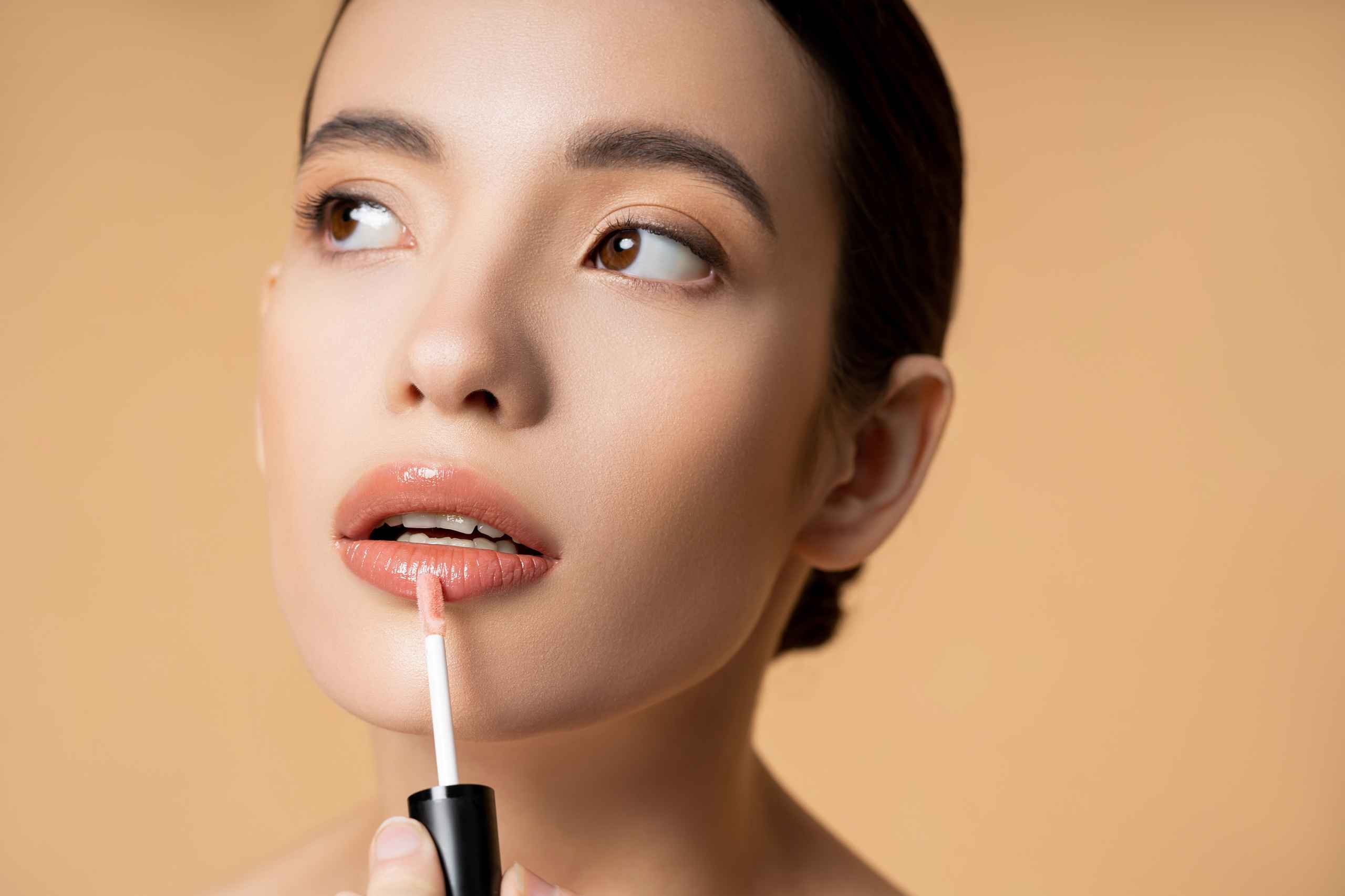 Portrait of young asian model applying lip gloss and looking awa